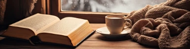 Buch, Tasse und Wolldecke am Fenster mit Blick auf winterliche Landschaft