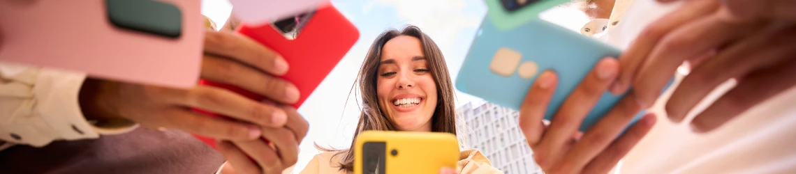 Fröhliches Mädchen schaut auf Smartphone. Gruppe von Freunden mit Handys