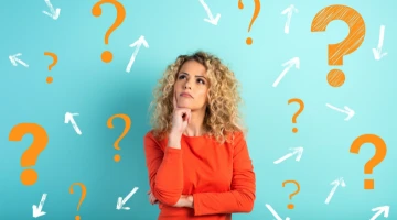 Junge Frau steht vor einer Wand mit vielen Fragezeichen