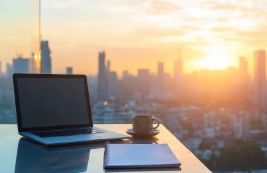 Laptop auf Glastisch mit Blick auf die städtische Skyline von einer Hochhauswohnung aus